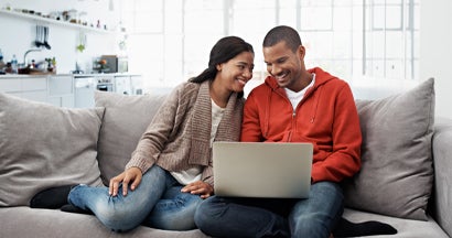 Smiling young couple sitting on their sofa using a laptop. Car Insurance Reviews.