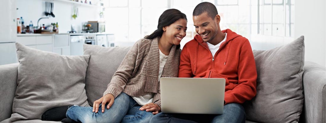 Smiling young couple sitting on their sofa using a laptop. Car Insurance Reviews.