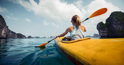 Woman exercising and exploring calm tropical bay by kayak.